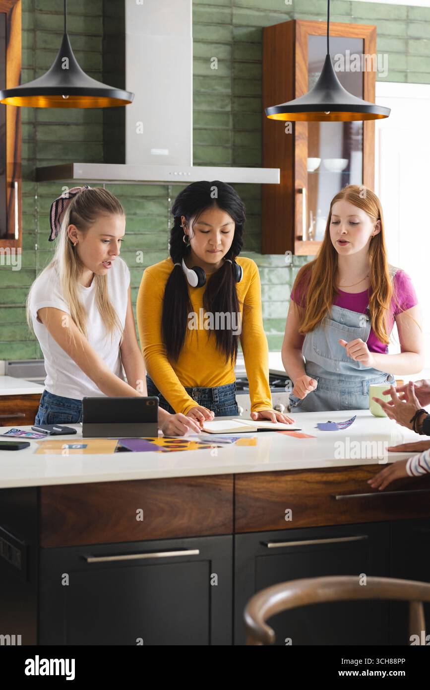 Adolescentes collaborant sur un projet scolaire dans une cuisine moderne, discutant des idées Banque D'Images