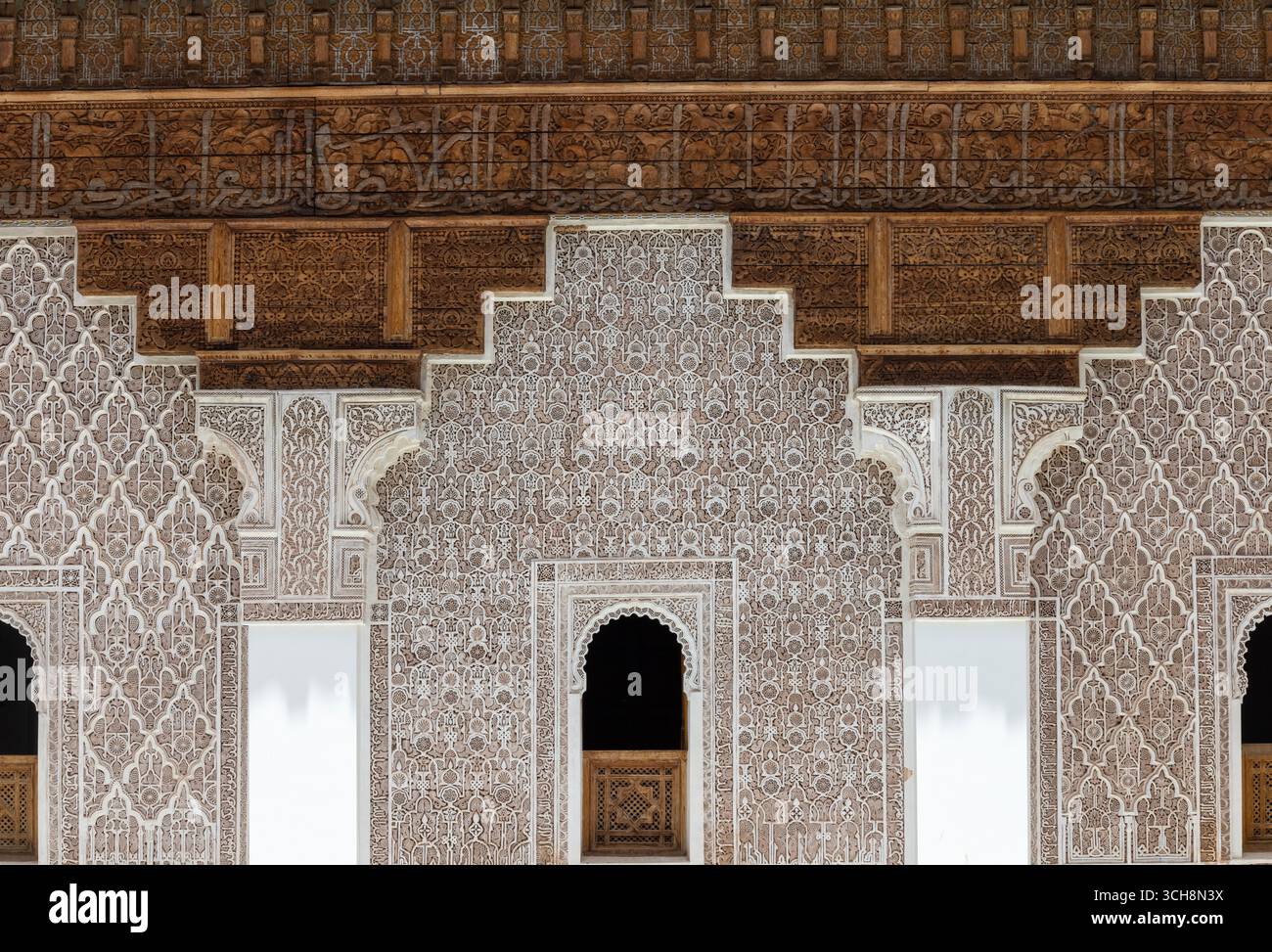 Stuc sculpté et frise de cèdre avec calligraphie arabe et petites fenêtres cintrées sur le mur de la cour de Ben Youssef Madrasa (Medersa Ben Youssef) Banque D'Images