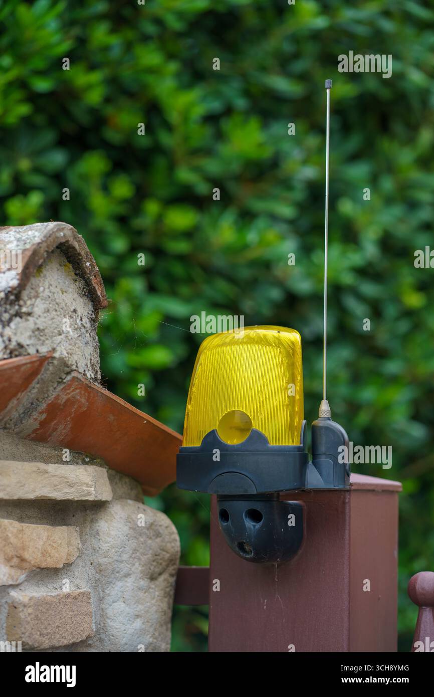 Une lampe de signalisation jaune avec une antenne sur une clôture en pierre sur un jardin verdoyant. Lampe de signalisation jaune dans une maison privée. Banque D'Images