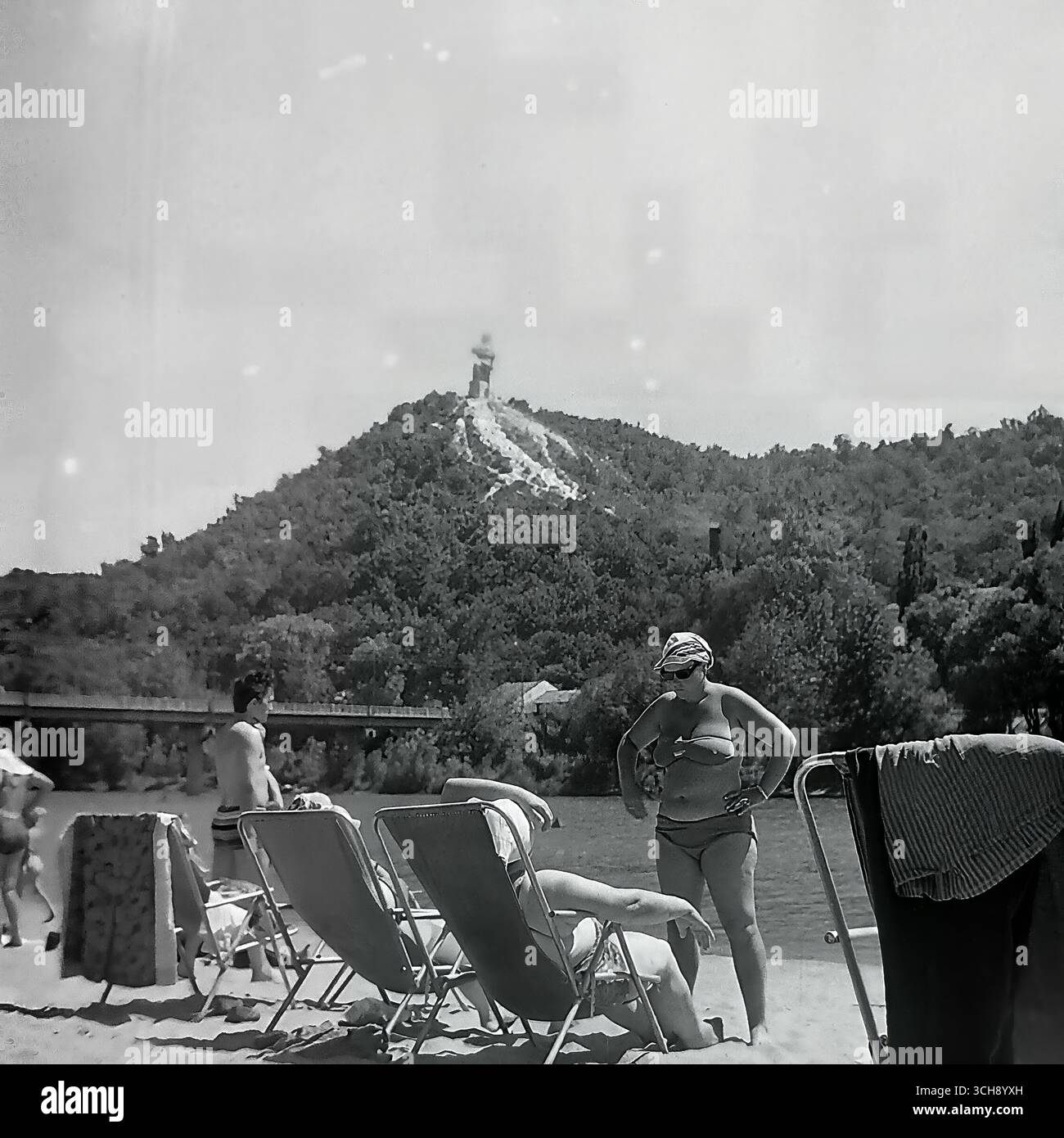 Une scène classique de vacances d'été sur la plage de Sviatohirsk pendant les années 1970-80 Les vacanciers prennent le soleil dans des chaises longues sur la rive de la rivière Seversky Donets, avec la célèbre vue sur la montagne et la statue monumentale d'Artem en arrière-plan. La photographie est un document vivant de la culture soviétique de la station balnéaire et crée une image nostalgique d'un été insouciant et paisible. La photo capture le contraste unique entre les loisirs quotidiens et l'idéologie monumentale qui est devenue une partie du paysageA scène classique des vacances d'été sur la plage de Sviatohirsk dans les années 1970-80 Vacanciers s Banque D'Images Une scène classique de vacances d'été sur la plage de Sviatohirsk pendant les années 1970-80 Les vacanciers prennent le soleil dans des chaises longues sur la rive de la rivière Seversky Donets, avec la célèbre vue sur la montagne et la statue monumentale d'Artem en arrière-plan. La photographie est un document vivant de la culture soviétique de la station balnéaire et crée une image nostalgique d'un été insouciant et paisible. La photo capture le contraste unique entre les loisirs quotidiens et l'idéologie monumentale qui est devenue une partie du paysageA scène classique des vacances d'été sur la plage de Sviatohirsk dans les années 1970-80 Vacanciers s Banque D'Images