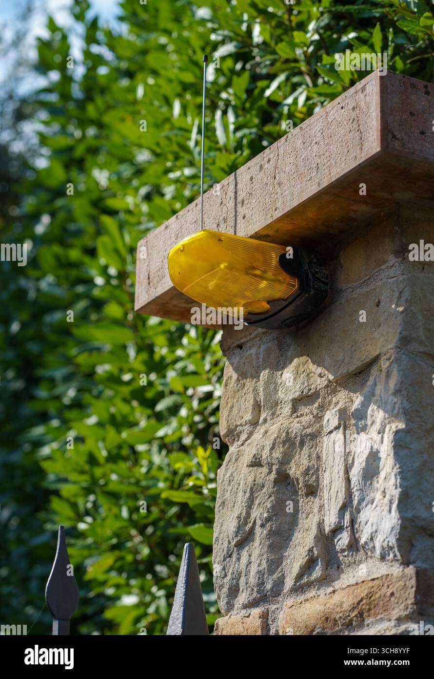 Une lampe de signalisation jaune avec une antenne sur une clôture en pierre sur un jardin verdoyant. Lampe de signalisation jaune dans une maison privée. Banque D'Images