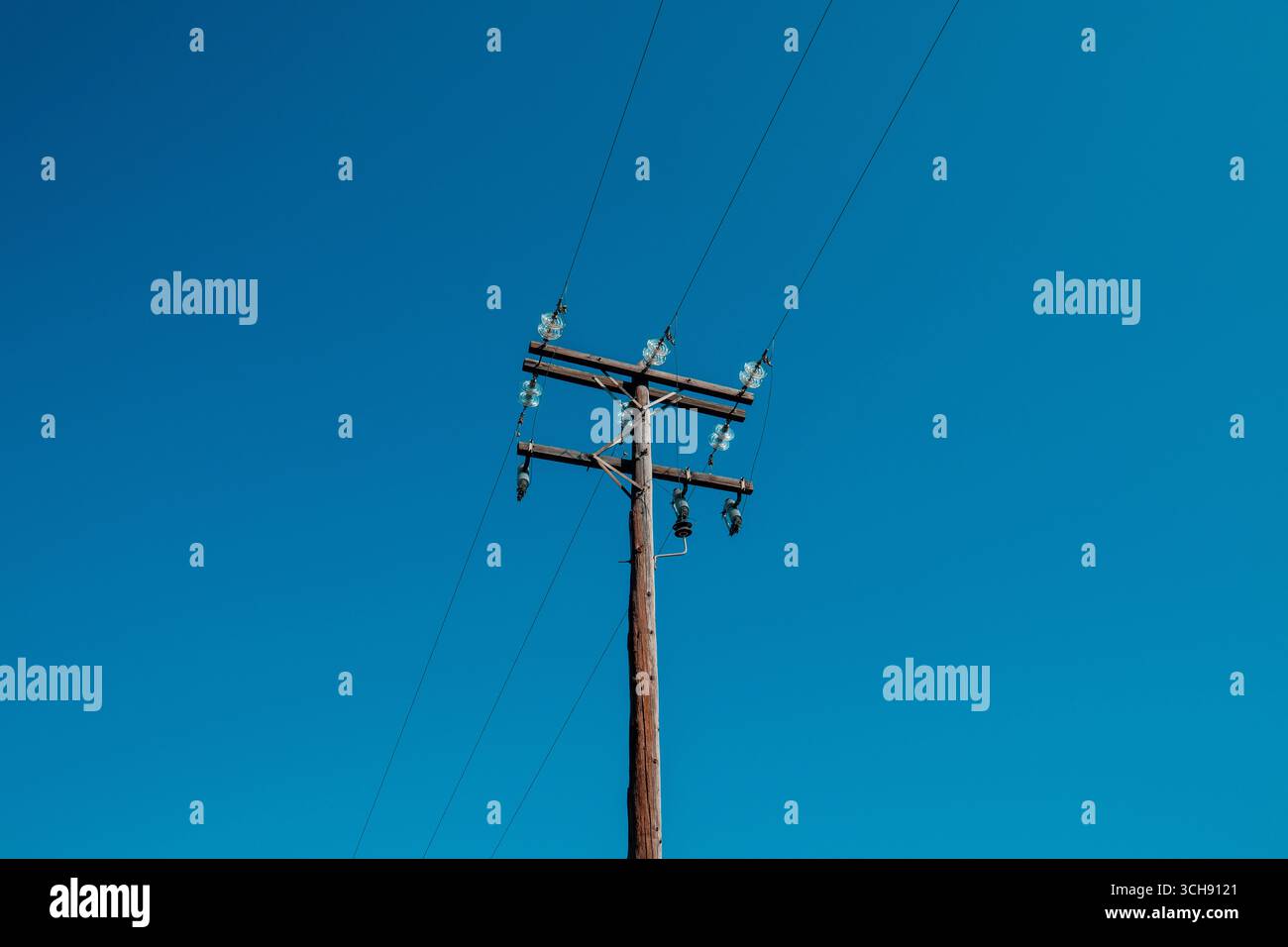 Poteau électrique en bois avec plusieurs lignes électriques et isolateurs de verre, placé contre un ciel bleu clair et vibrant. Mise au point sélective. Banque D'Images