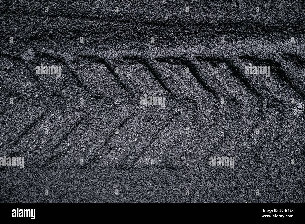 Gros plan des marques de la bande de roulement des pneus d'un tracteur imprimées sur une surface d'asphalte rugueuse, créant une texture industrielle et un motif abstrait. Vue de dessus. Banque D'Images