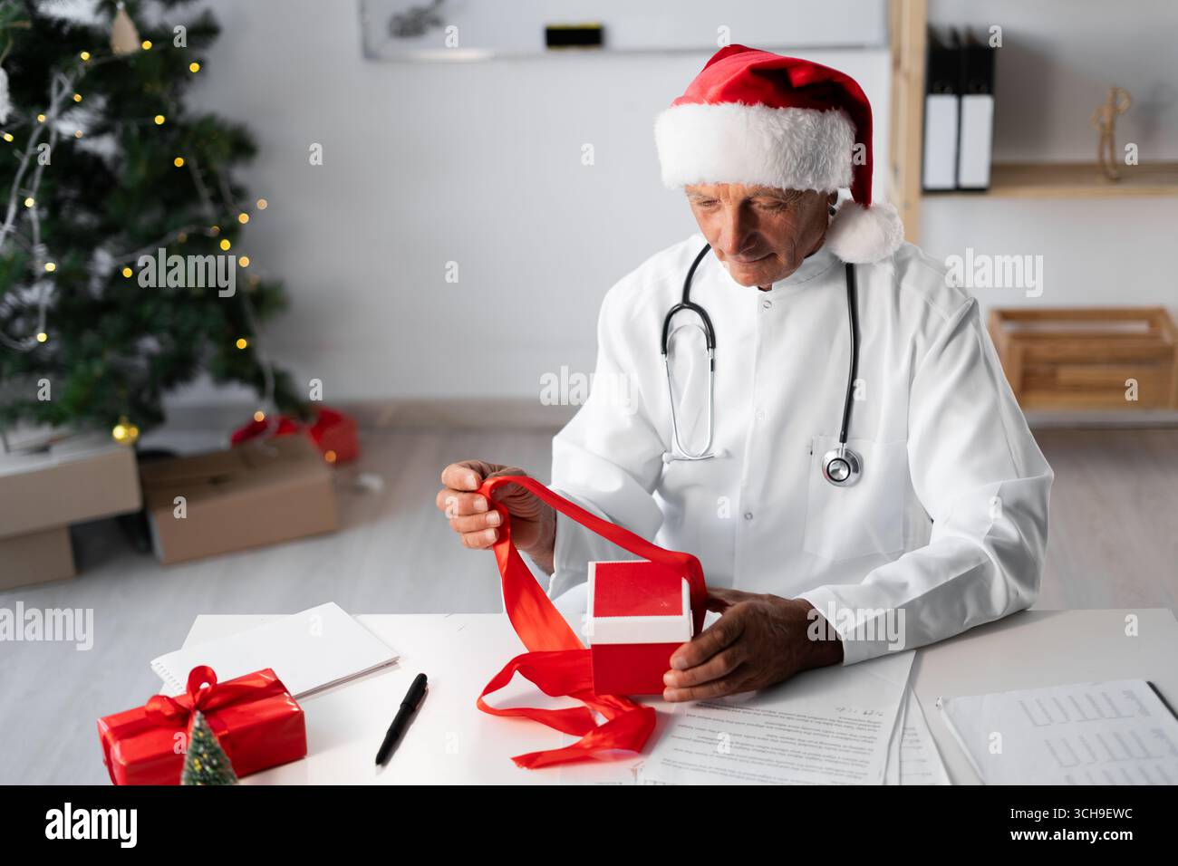 Médecin âgé senior dans le chapeau de Santa avec boîte-cadeau sur le quart de travail à l'hôpital la veille de Noël. copier l'espace Banque D'Images