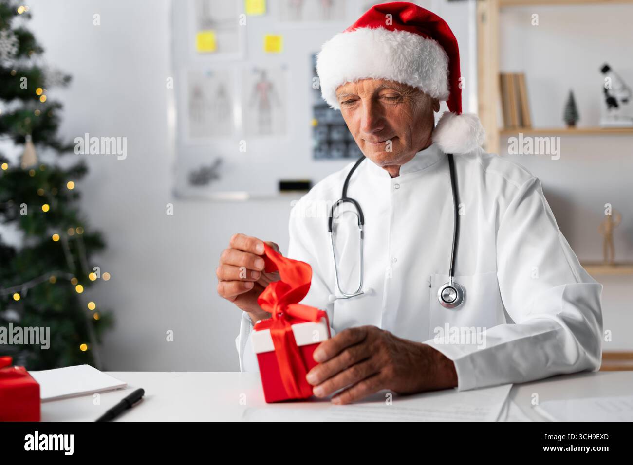 Médecin âgé senior dans le chapeau de Santa avec boîte-cadeau sur le quart de travail à l'hôpital la veille de Noël. copier l'espace Banque D'Images
