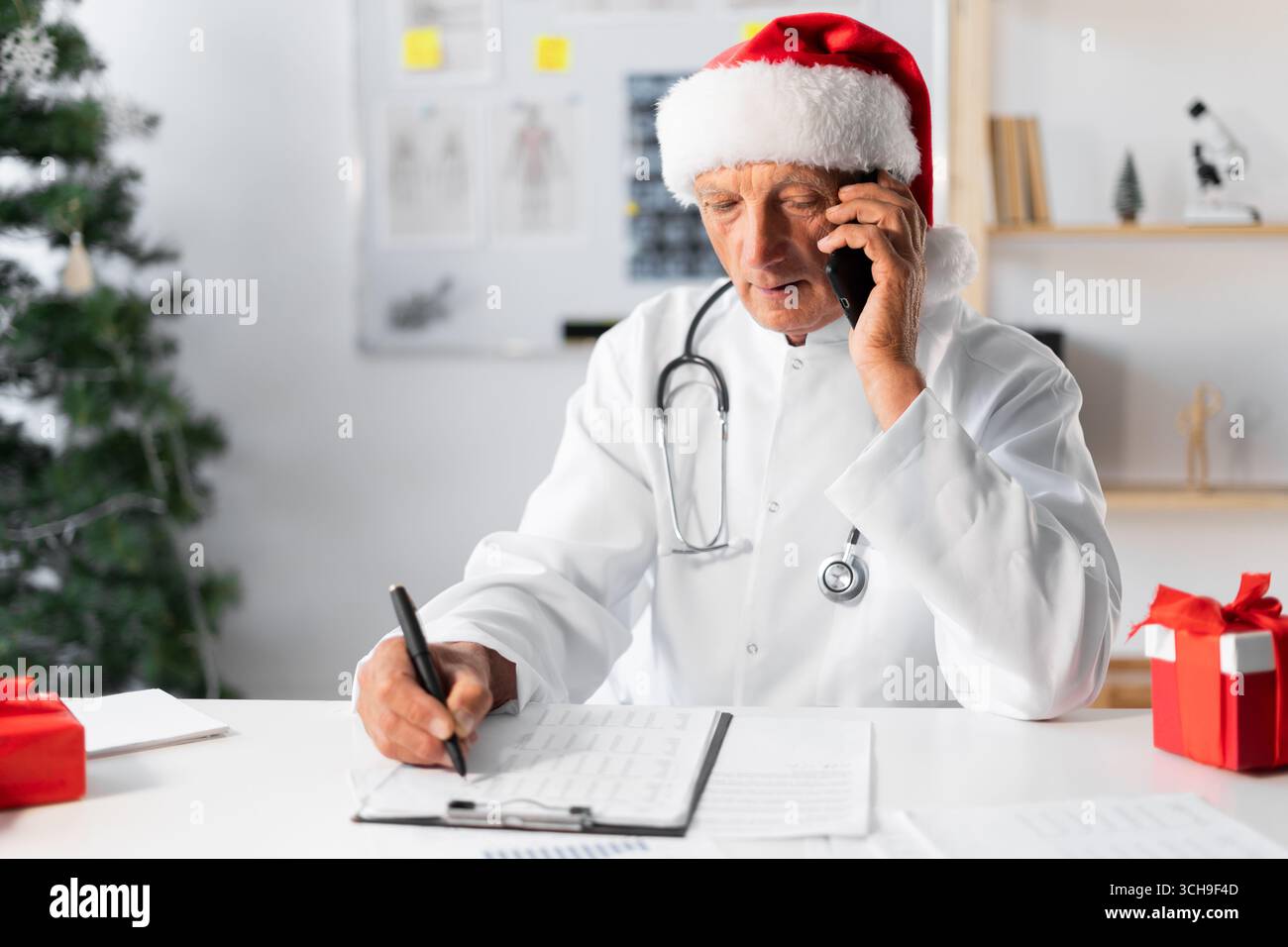 Médecin âgé senior à Santa Hat consultant le patient dans la conversation téléphonique professionnel des soins de santé sur le quart de travail à l'hôpital la veille de Noël. moyen Banque D'Images