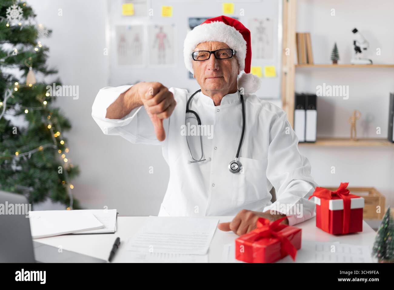 Mécontenté, le médecin aîné senior en chapeau de Père Noël pendant le quart de travail de la veille de noël montrant un geste d'aversion du pouce vers le bas. copier l'espace Banque D'Images