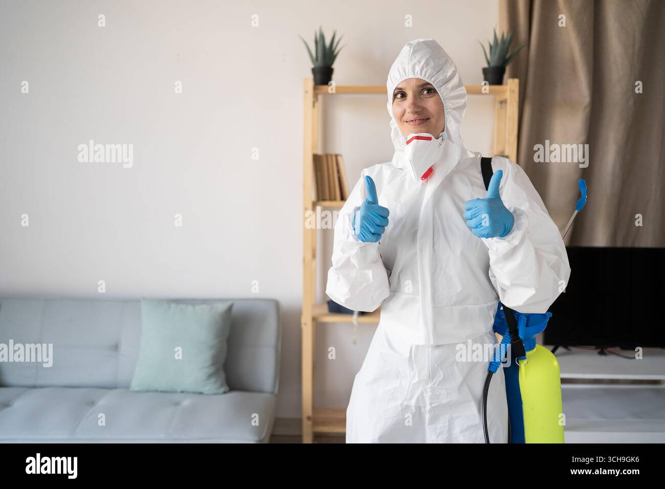 Exterminateur féminin du service de lutte antiparasitaire travaillant à l'intérieur de la maison avec bouteille de pulvérisateur faisant le geste du pouce vers le haut à la maison. copier l'espace Banque D'Images