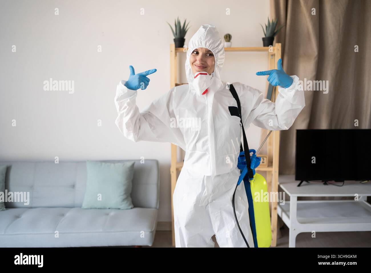 Assuré. Exterminateur féminin du service de lutte antiparasitaire travaillant à l'intérieur de la maison avec la bouteille de pulvérisateur, pointant les doigts à soi-même à la maison. Choisir Me. Banque D'Images