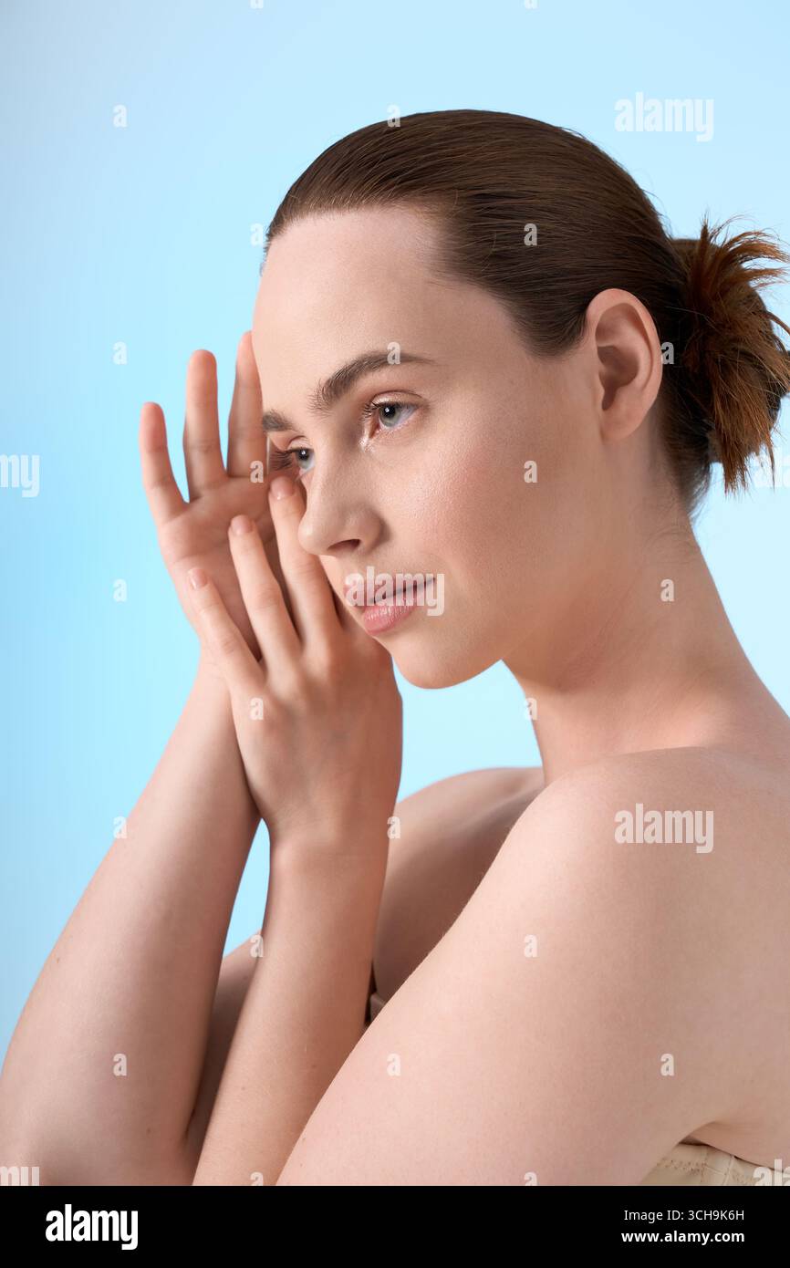 Jeune femme à la mode avec une pose élégante transmet la tranquillité sur un fond bleu apaisant. Banque D'Images