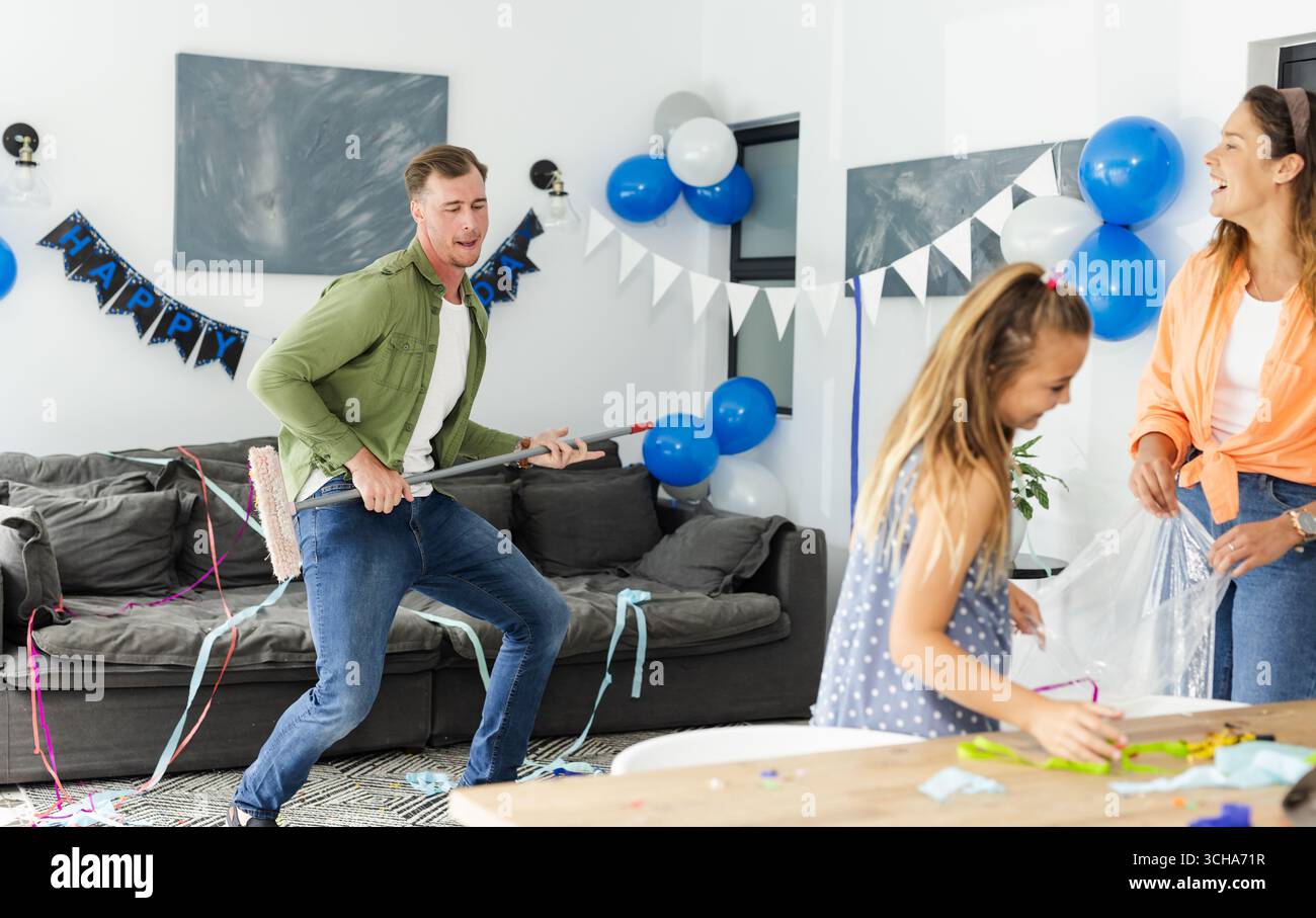 Père dansant avec balai tandis que fille et mère décorant pour la fête à la maison. Célébration, famille, festif, heureux, liaison, joyeux Banque D'Images