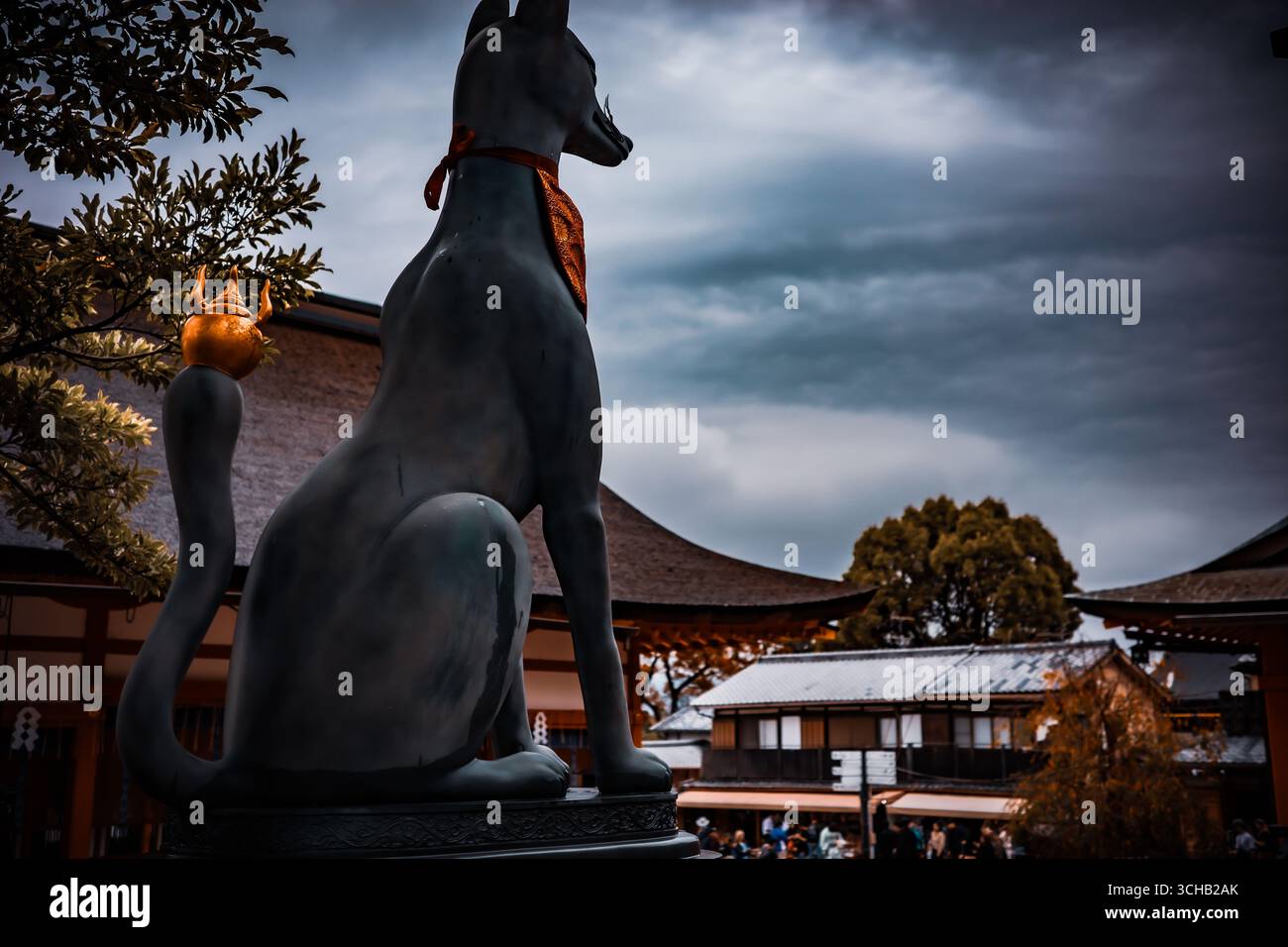 Statue de renard en pierre avec ornement symbolique dans un sanctuaire japonais sous un ciel nuageux dramatique à Fushimi Inari-taisha, Kyoto, Japon. Banque D'Images