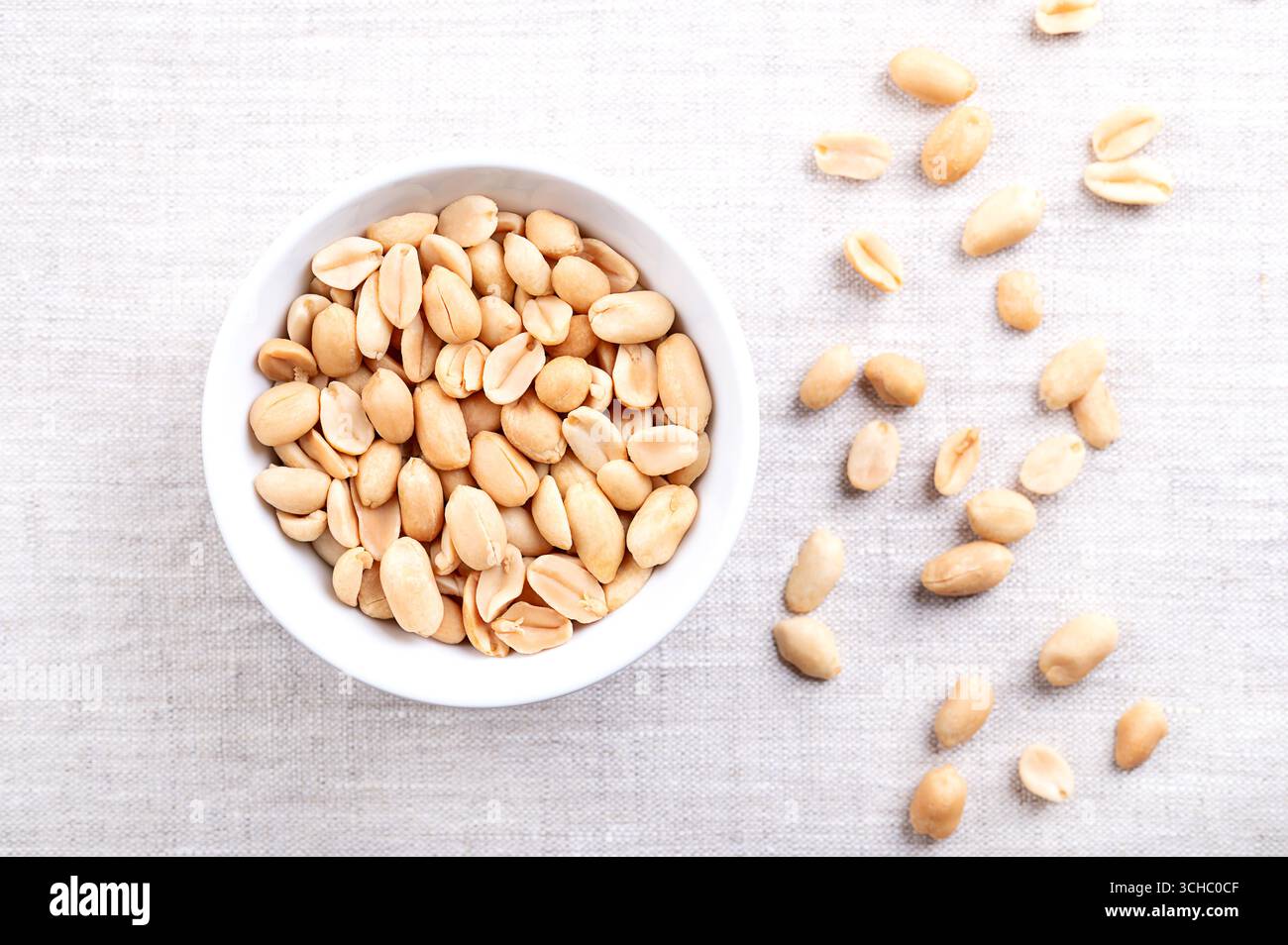 Cacahuètes rôties dans un bol blanc sur tissu de lin. Snack croquant prêt-à-manger à base de fruits d'Arachis hypogaea. Noix de grignotage dorées légères. Banque D'Images