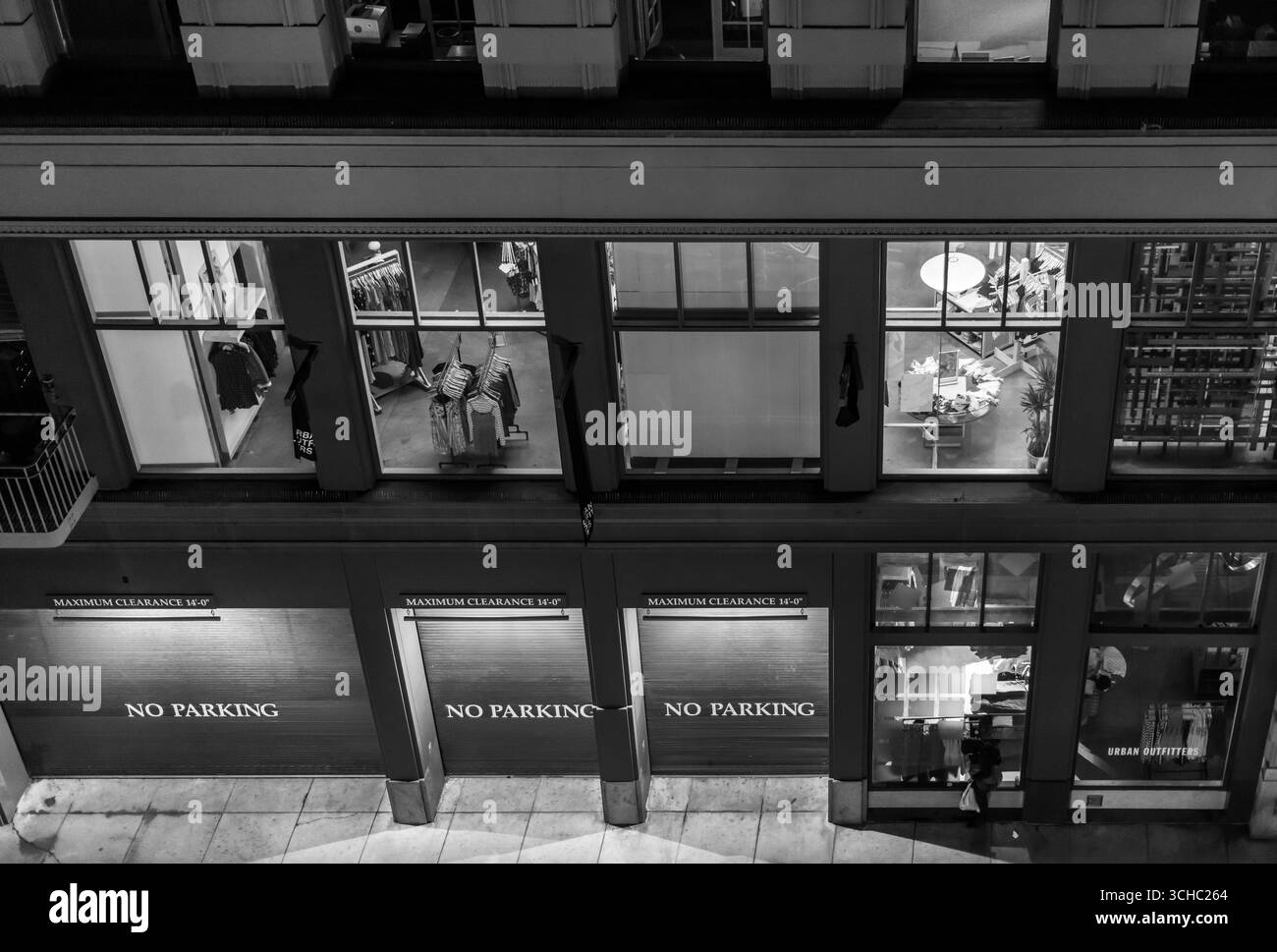 Photo en noir et blanc montrant une personne sans-abri devant un centre commercial haut de gamme à San Francisco, mettant en évidence les inégalités urbaines. Banque D'Images