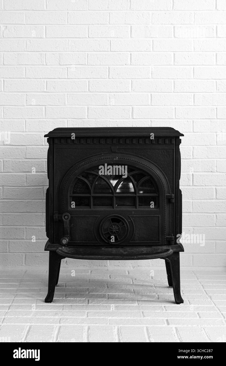 Un poêle à bois en fonte noire se tient contre un mur de briques blanches. Banque D'Images