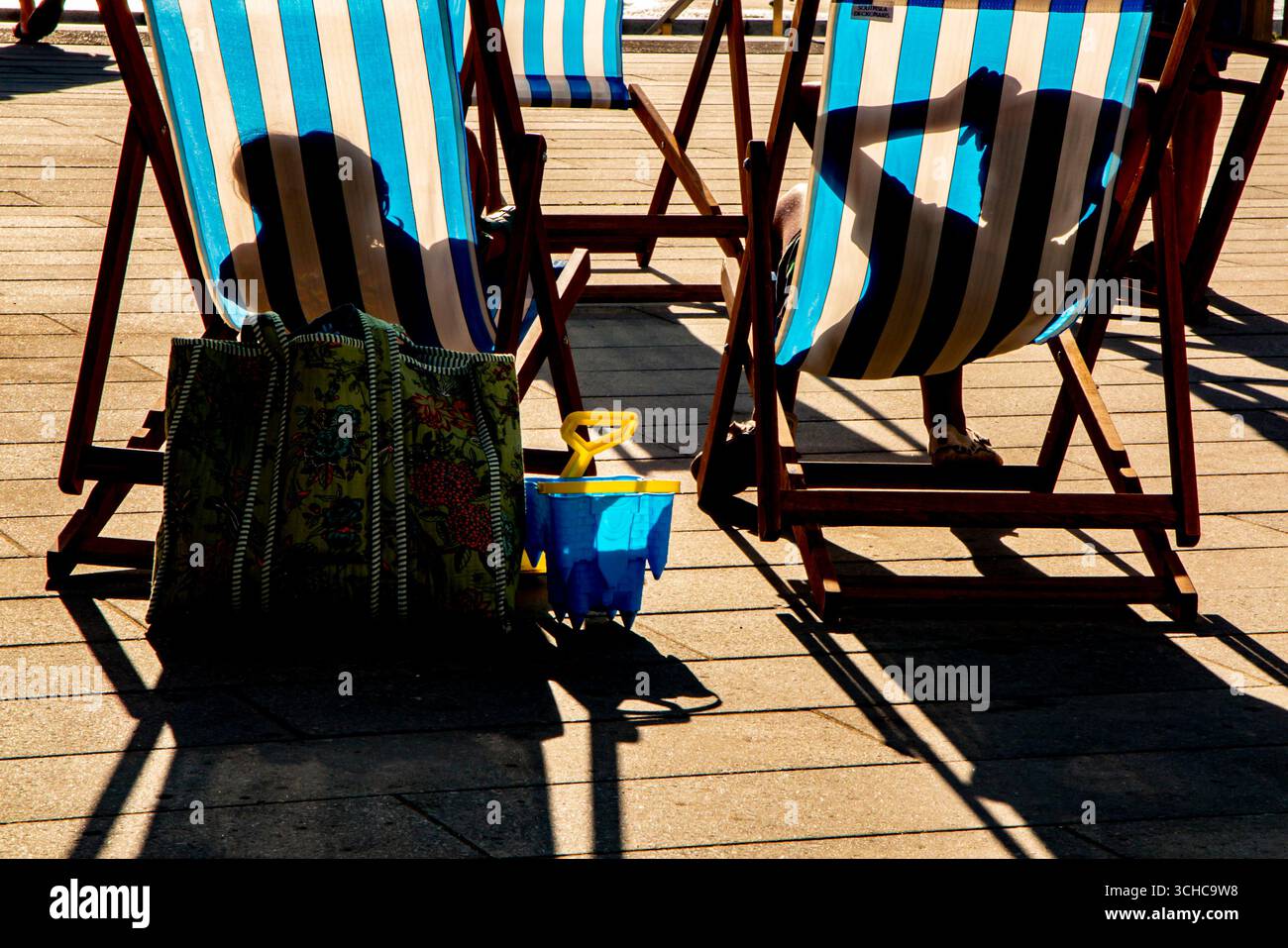 Allongé au soleil dans des transats rayés dans une station balnéaire anglaise Banque D'Images