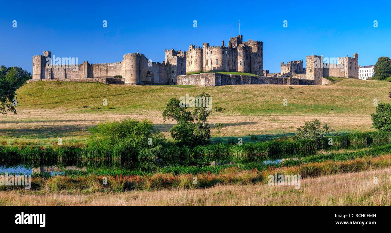Une vue à l'aube par une journée ensoleillée en été du château d'Alnwick reflétée dans la rivière ALN vue depuis les pâturages Banque D'Images