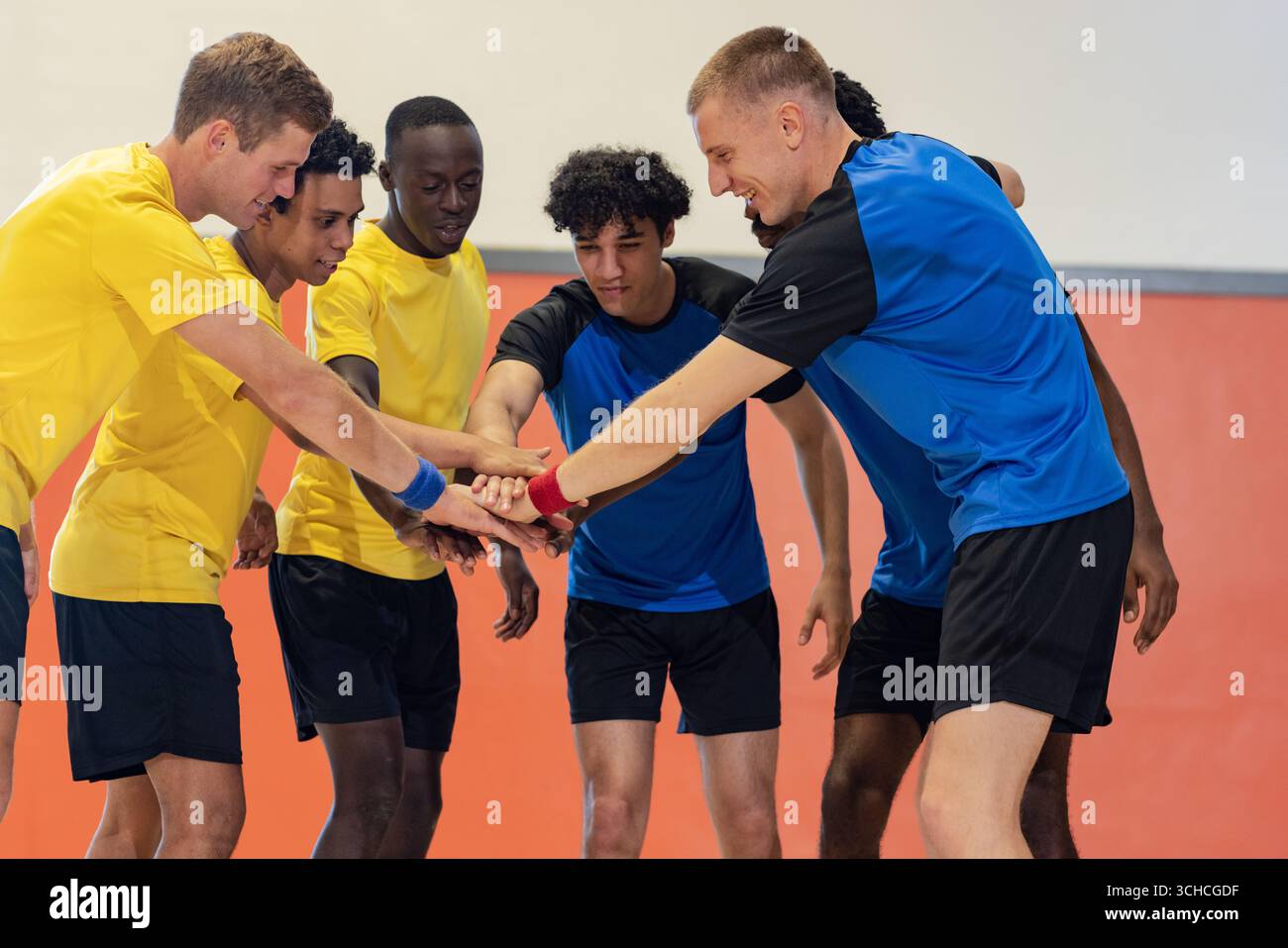 Divers athlètes masculins se blottissant en plaçant les mains au centre dans le gymnase portant des maillots jaunes et bleus. Coéquipiers, travail d'équipe, sport, fitness, motivation, Banque D'Images Divers athlètes masculins se blottissant en plaçant les mains au centre dans le gymnase portant des maillots jaunes et bleus. Coéquipiers, travail d'équipe, sport, fitness, motivation, Banque D'Images