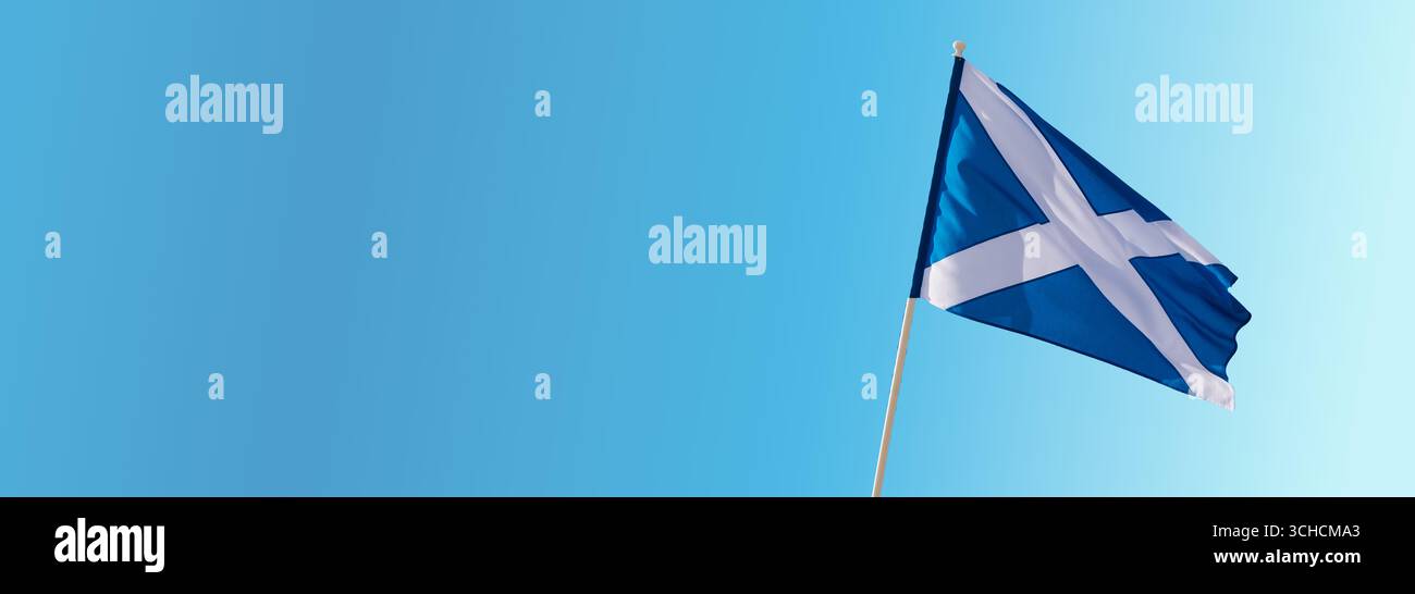 Le drapeau national de l’Écosse, le Saltire ou encore la Croix d’Andrew, volant sur un mât de drapeau contre un ciel bleu aux nuages éparpillés, symbolisant l’écossais Banque D'Images