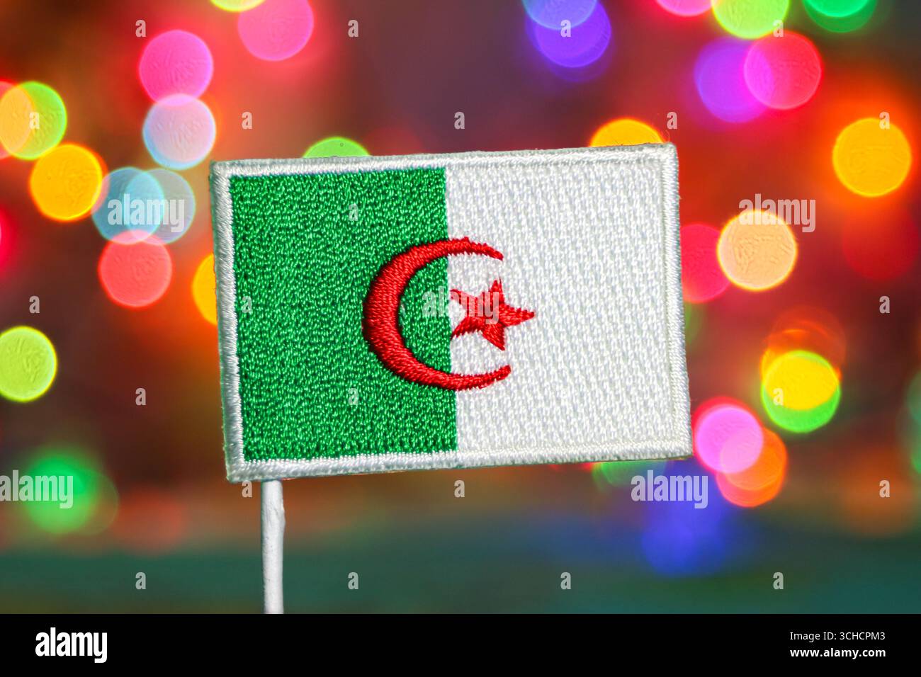 Broderie du drapeau algérien avec des feux d'artifice bokeh arc-en-ciel, symbolisant la célébration, la fête du nouvel an et la fierté nationale. Banque D'Images