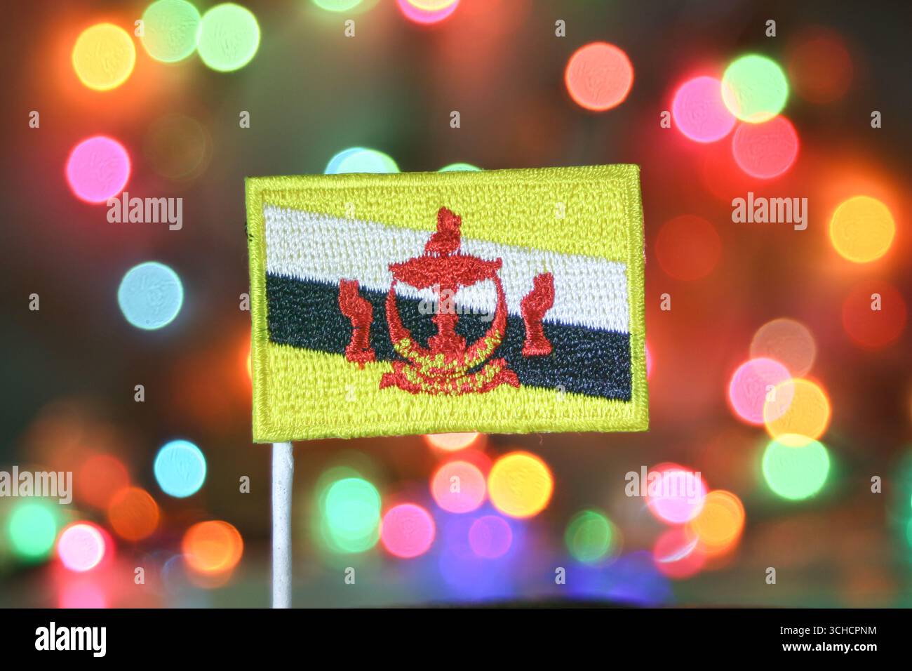 Brunei Darussalam drapeau brodé avec fond de feux d'artifice bokeh arc-en-ciel, symbolisant la célébration du nouvel an, la fierté nationale et la joie des fêtes. Banque D'Images