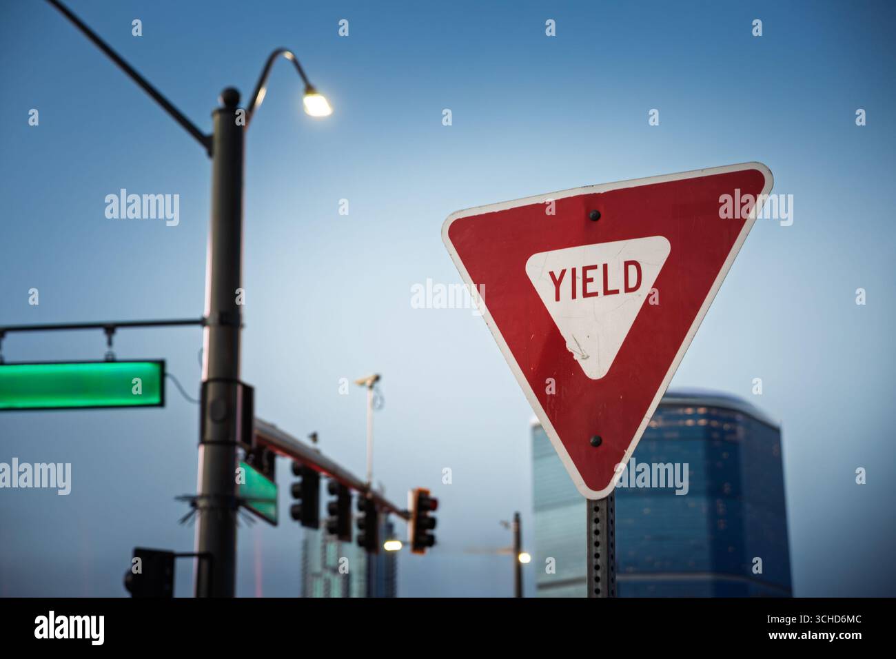Un panneau routier rouge et blanc triangulaire américain de rendement se trouve à une intersection éclairée en Amérique du Nord montrant une face réfléchissante altérée, des feux de circulation, Banque D'Images