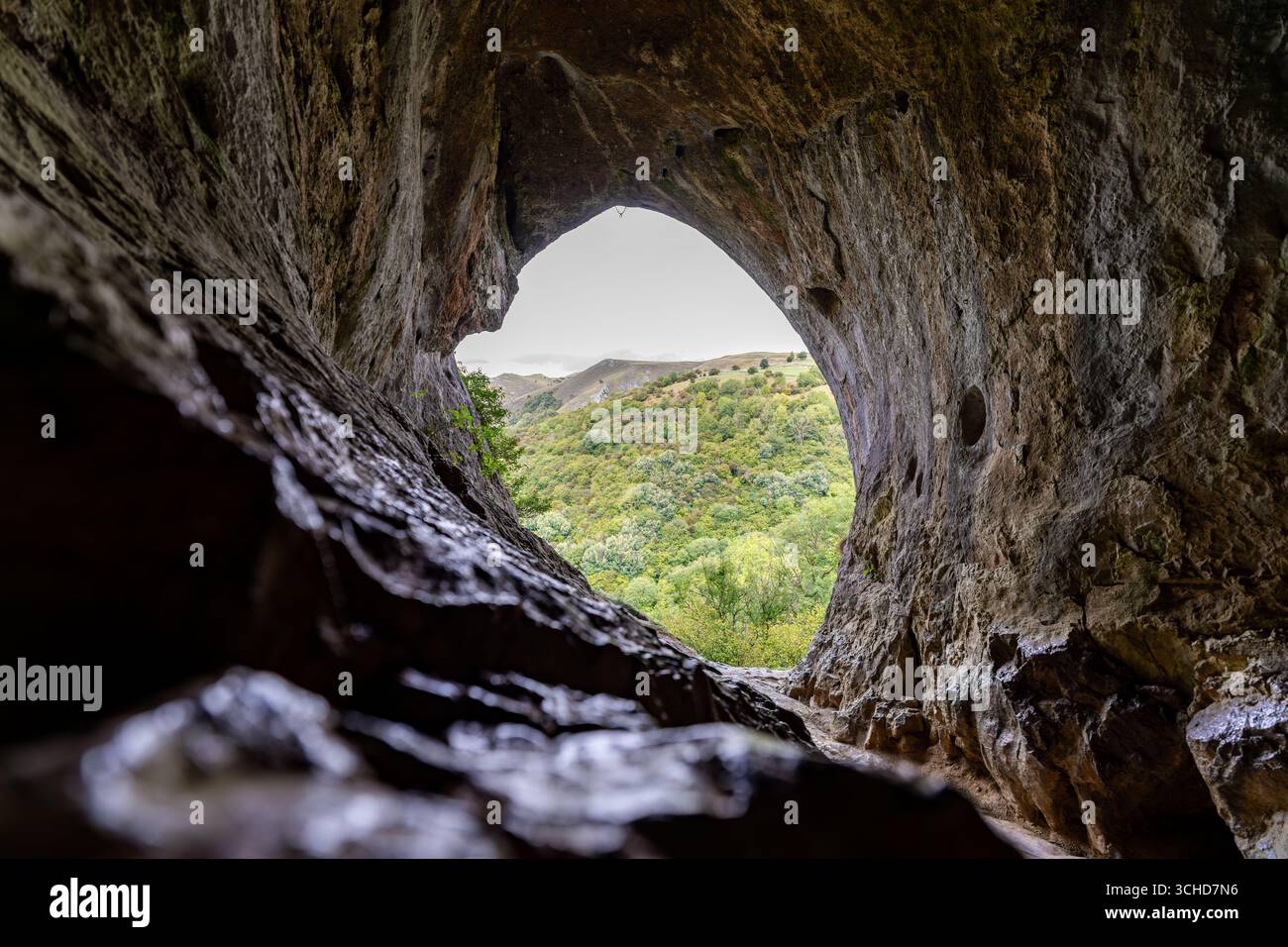 Ouverture de la grotte de roche naturelle encadrant une vue sur un paysage de vallée verdoyant, créant un contraste scénique entre l'intérieur sombre de la grotte et l'extérieur lumineux Banque D'Images