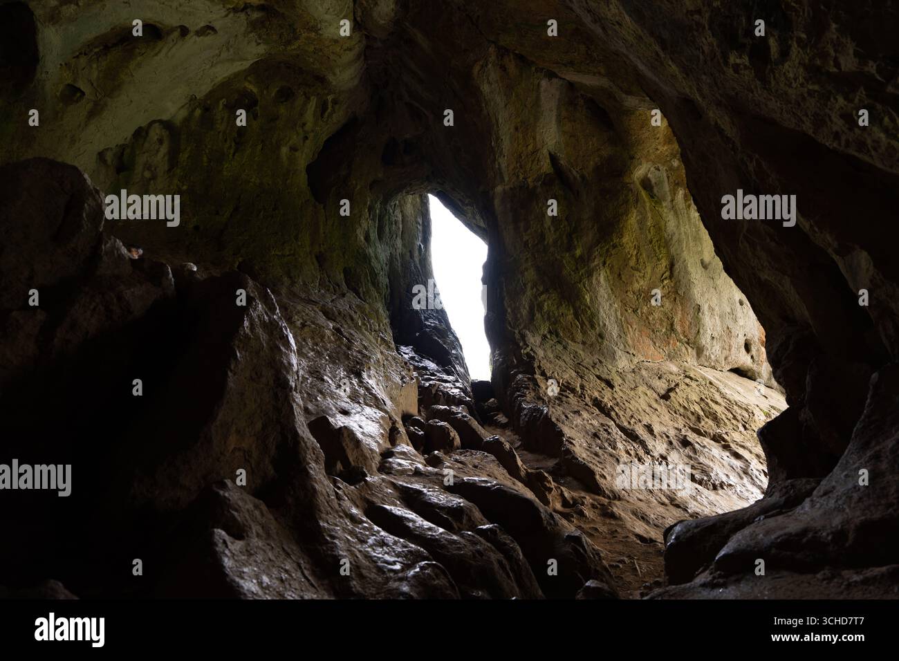 Lumière du soleil perçant à travers une ouverture étroite dans une grotte sombre, éclairant les formations rocheuses accidentées à l'intérieur Banque D'Images