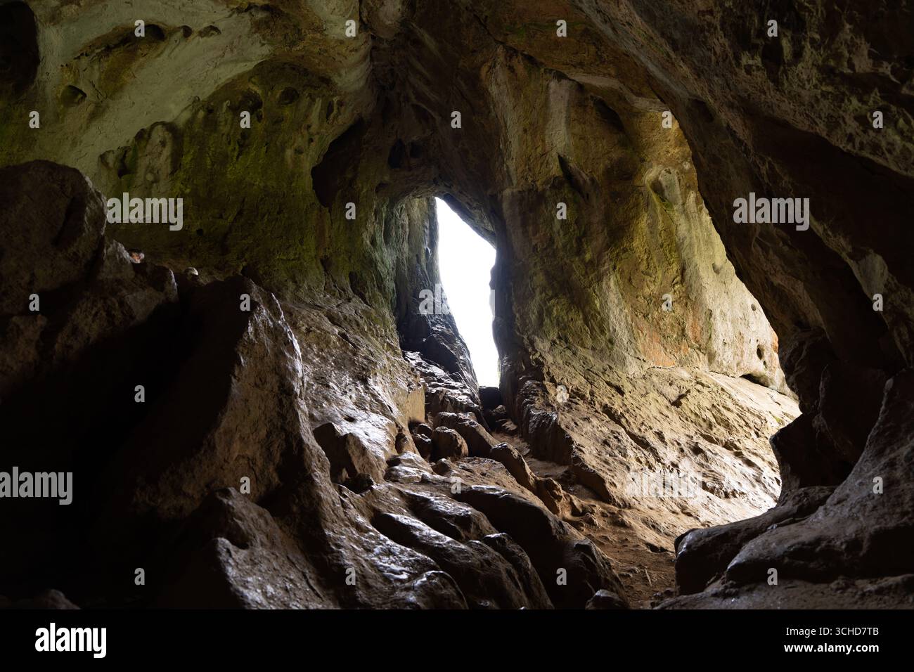 Lumière du soleil qui traverse une ouverture sombre de grotte, projetant une lumière chaude sur le sol rocheux et révélant la beauté du paysage souterrain Banque D'Images