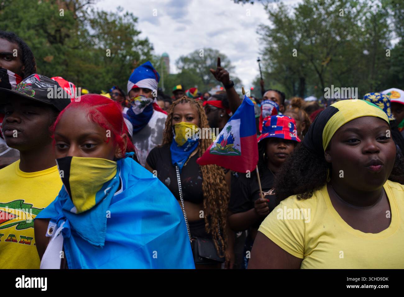 Une foule diversifiée de personnes, beaucoup portant des couvre-visage et tenant des drapeaux, semblent être à un événement extérieur. Banque D'Images