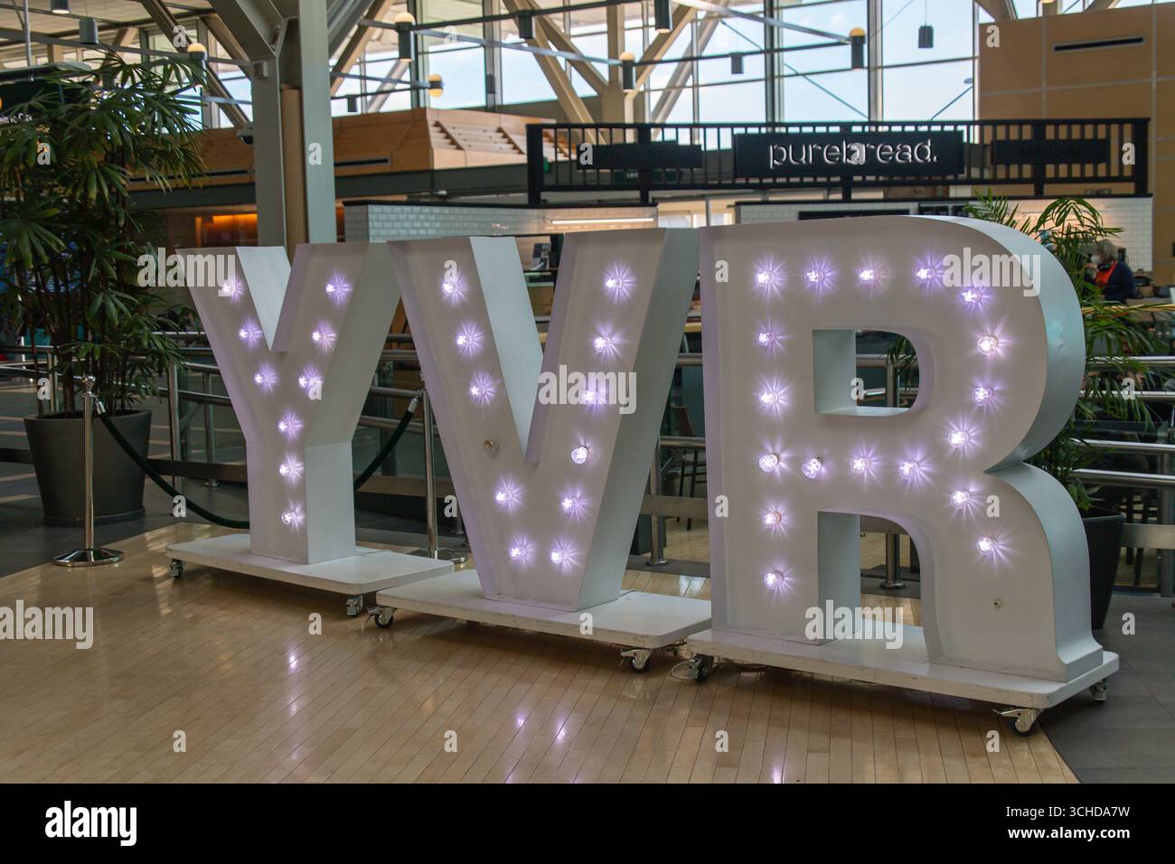 De grandes lettres YVR éclairées sont affichées à l'intérieur de l'aéroport international de Vancouver, près de l'aire de restauration, au décor moderne et à la lumière naturelle. Banque D'Images