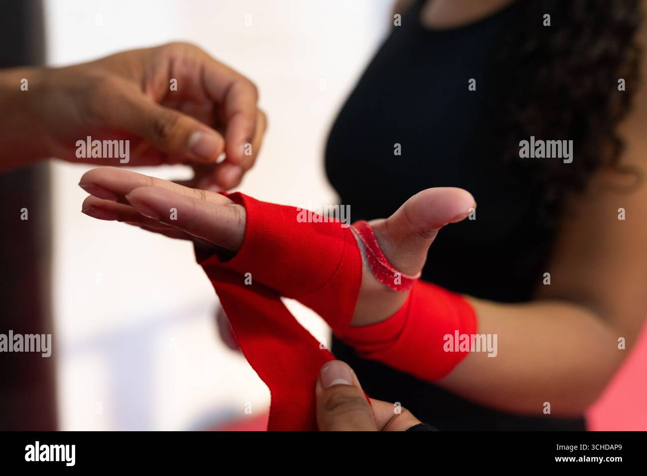Athlète féminine en haut sans manches noir avec entraîneur masculin enveloppant les mains rouges dans la salle de boxe Banque D'Images