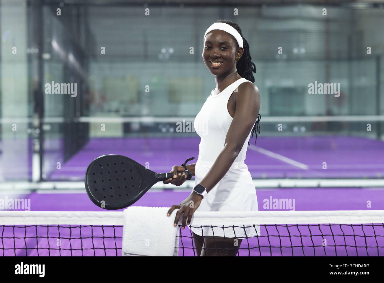 Femme afro-américaine tenant raquette noire avec serviette par filet sur court de padel en montre de sport Banque D'Images