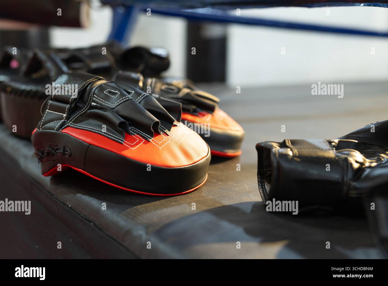 Les coussinets de boxe noirs et rouges reposent sur la plate-forme sous une corde à anneau bleue, montrant des coutures Banque D'Images