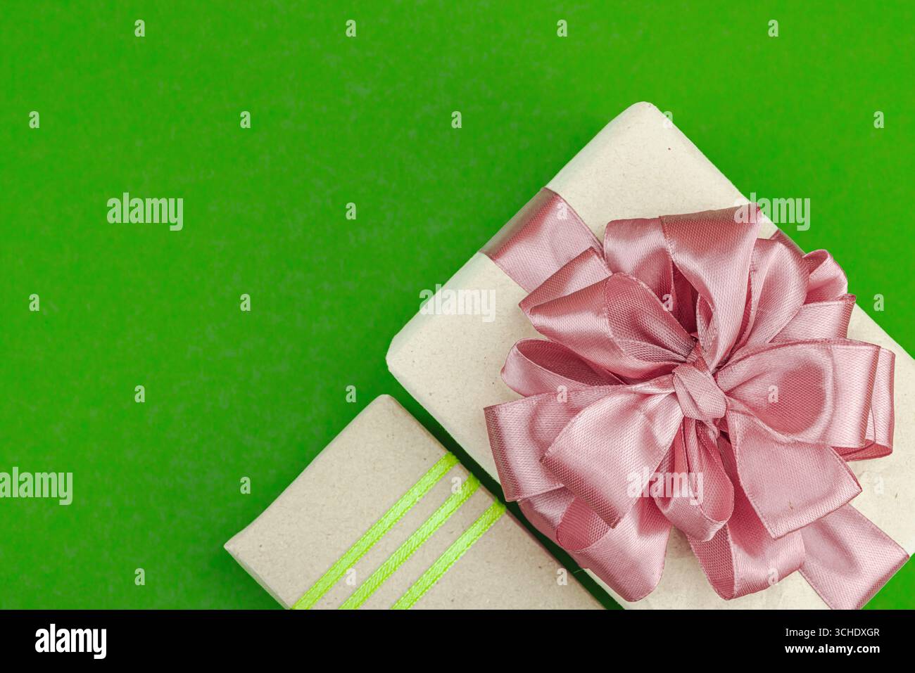 Boîtes-cadeaux écologiques enveloppées dans du papier kraft et décorées avec des rubans de satin sur fond vert. Concept de salutation, meilleurs voeux, plat, vue de dessus Banque D'Images