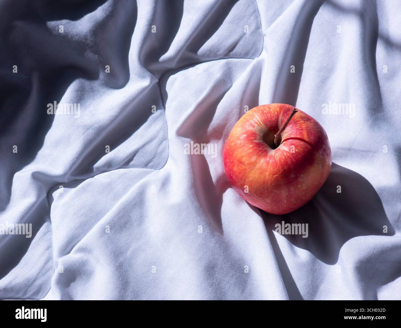 Pomme rouge mûre reposant sur un drap de lit doux et blanc, se prélasser à la lumière naturelle du soleil et créant une atmosphère accueillante et paisible parfaite pour une matinée sereine Banque D'Images