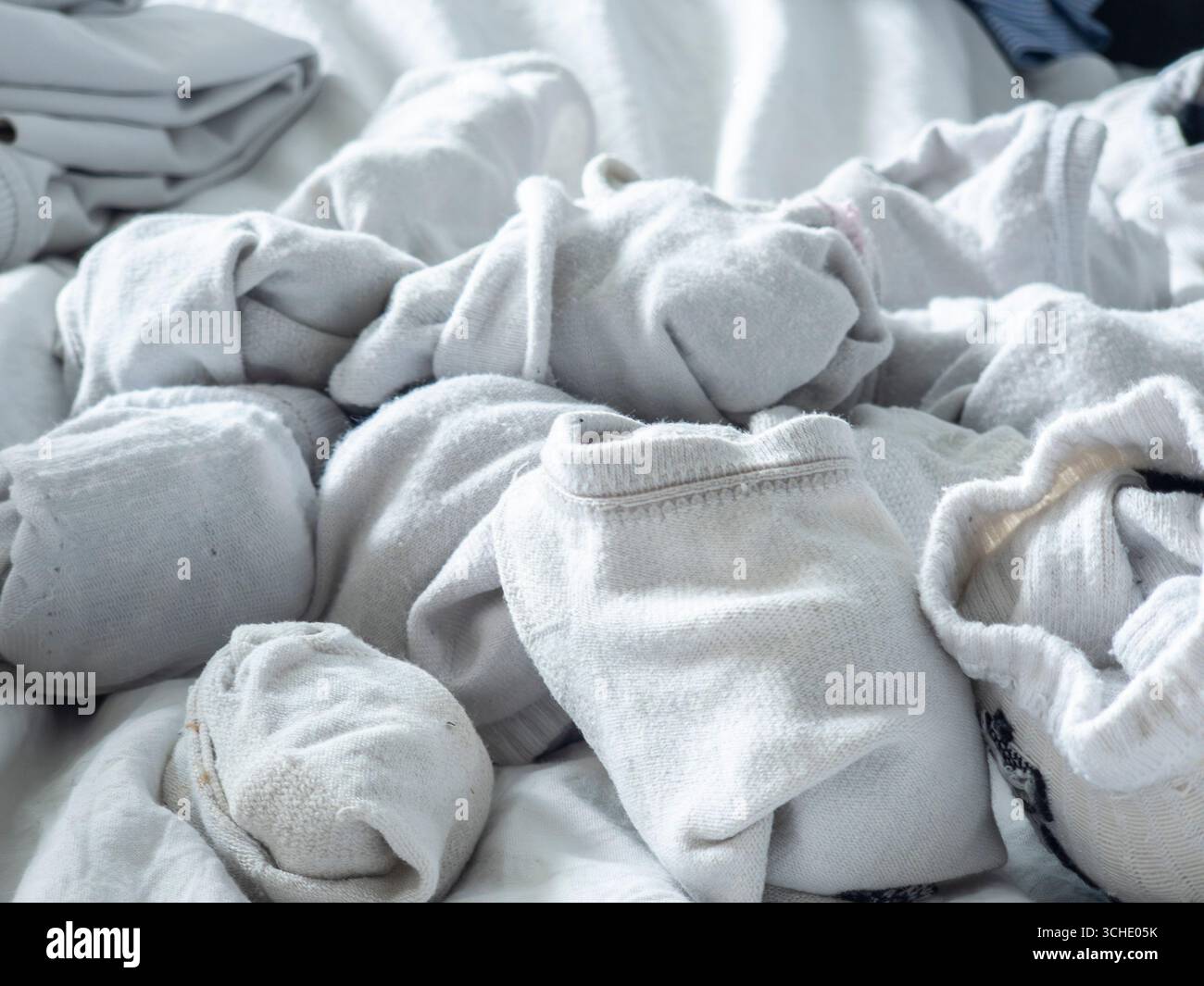 Chaussettes blanches enroulées et vêtements dispersés sur un drap de lit blanc créent une composition abstraite, mettant en valeur des textures intrigantes, des plis, et un confortable, Banque D'Images