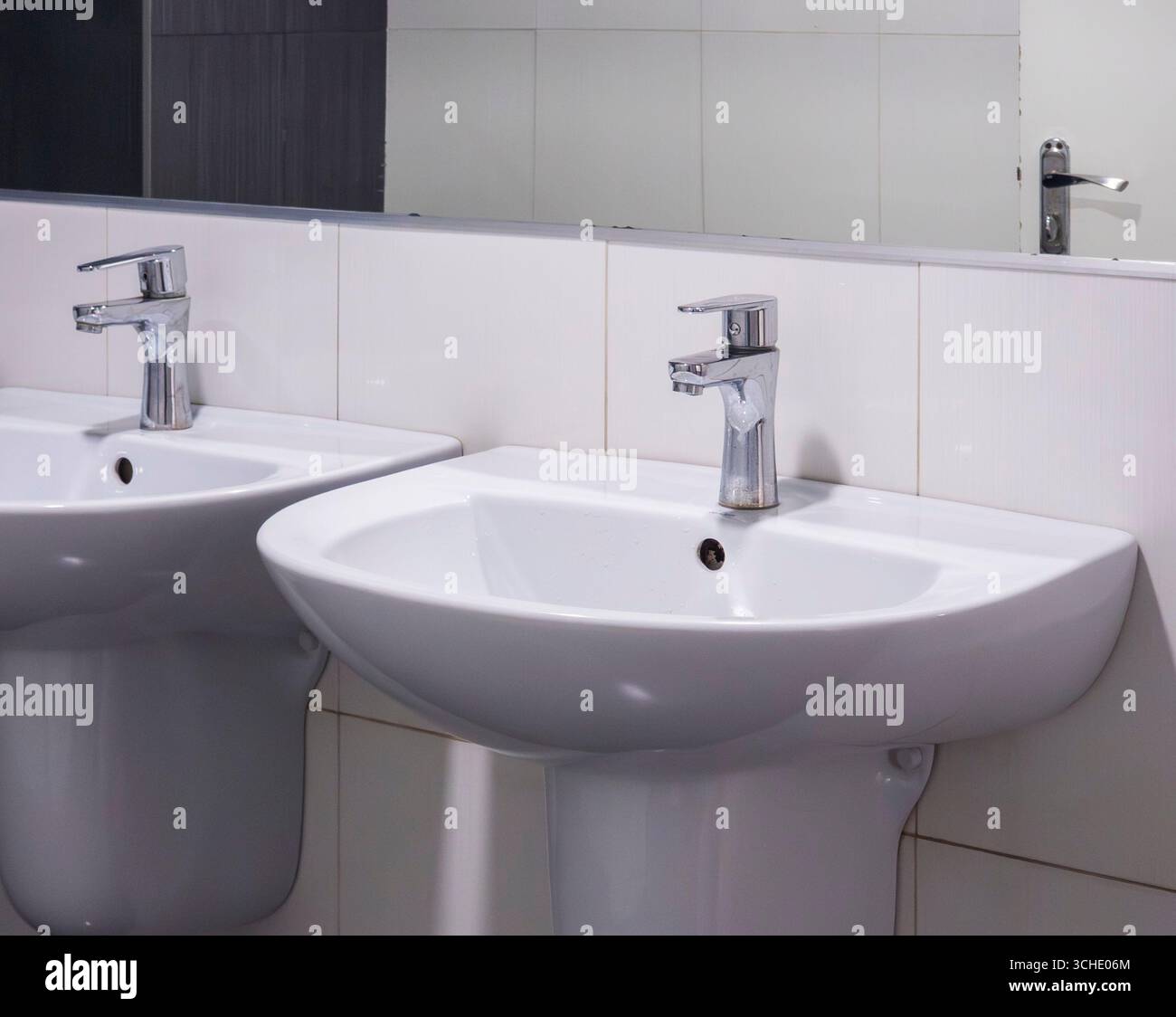 Deux lavabos en céramique blanc étincelants se tiennent côte à côte, leurs robinets modernes en chrome ajoutant une touche d'élégance aux toilettes publiques, reflétée dans le m Banque D'Images