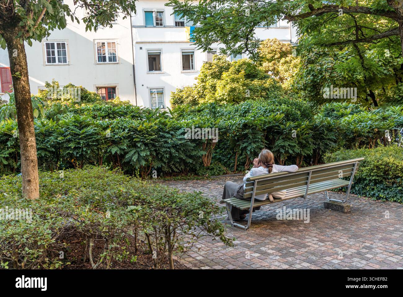 Femme vue de derrière se détendre dans un petit jardin le long de Spiegelgasse dans la vieille ville historique de Zurich, Suisse. Banque D'Images