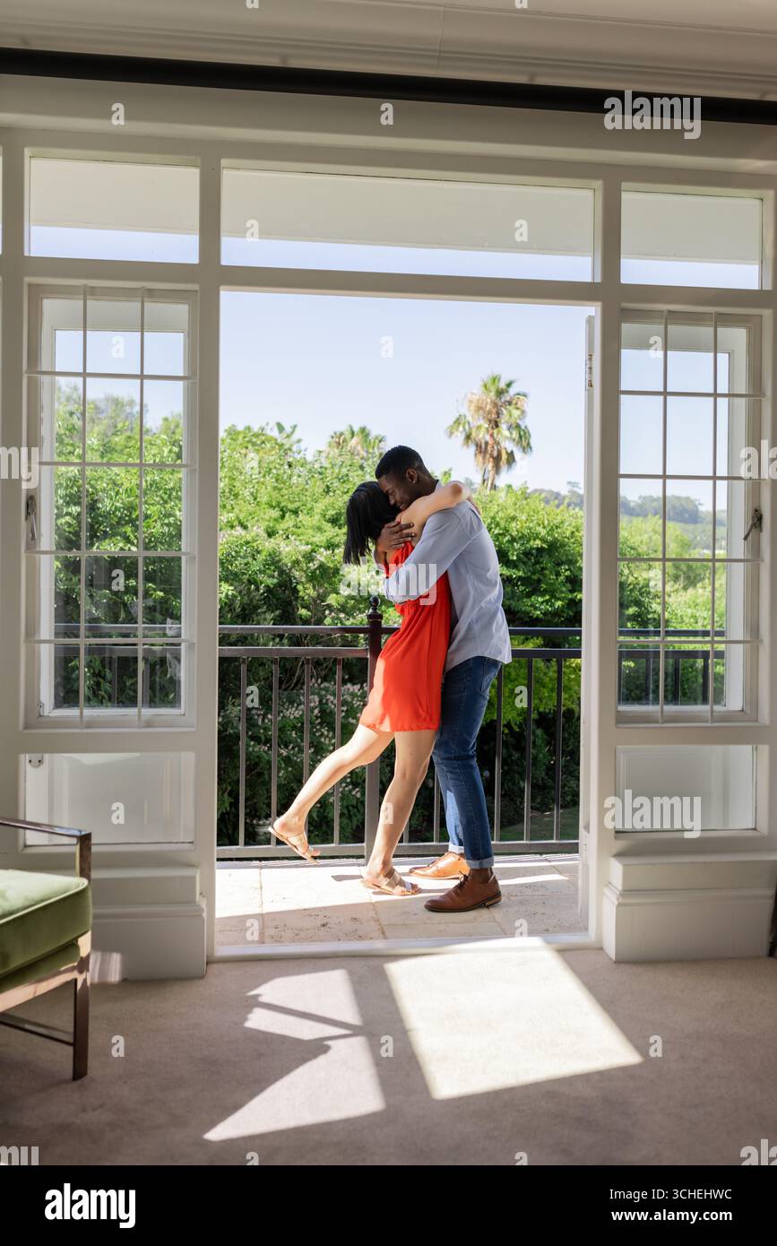 Embrasser un couple diversifié debout dans la porte ouverte du salon, avec des portes françaises encadrées blanches Banque D'Images Embrasser un couple diversifié debout dans la porte ouverte du salon, avec des portes françaises encadrées blanches Banque D'Images