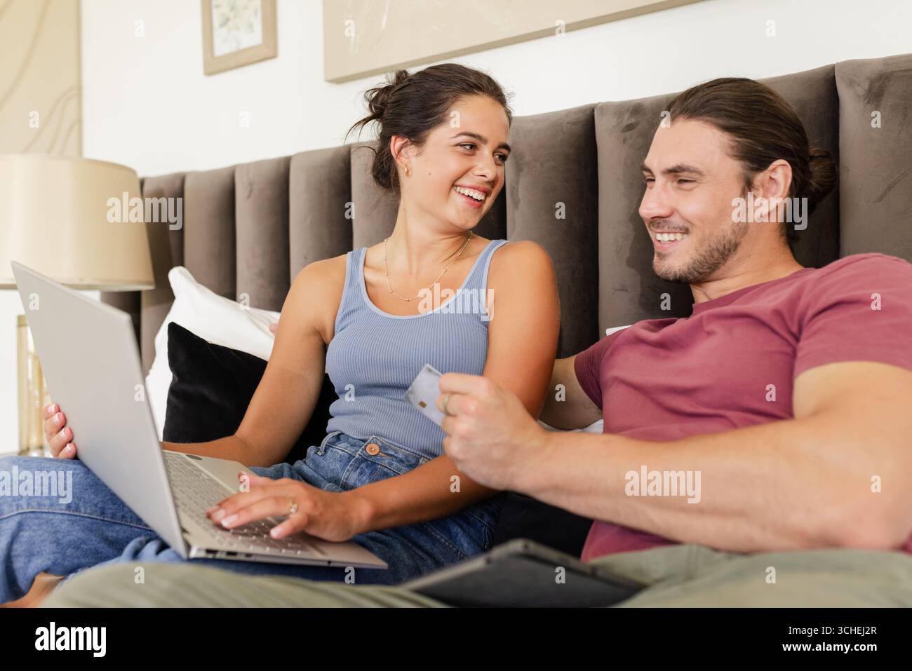Parcourir couple faisant l'achat en ligne sur lit rembourré, avec carte de crédit d'ordinateur portable et lampe de chevet Banque D'Images Parcourir couple faisant l'achat en ligne sur lit rembourré, avec carte de crédit d'ordinateur portable et lampe de chevet Banque D'Images