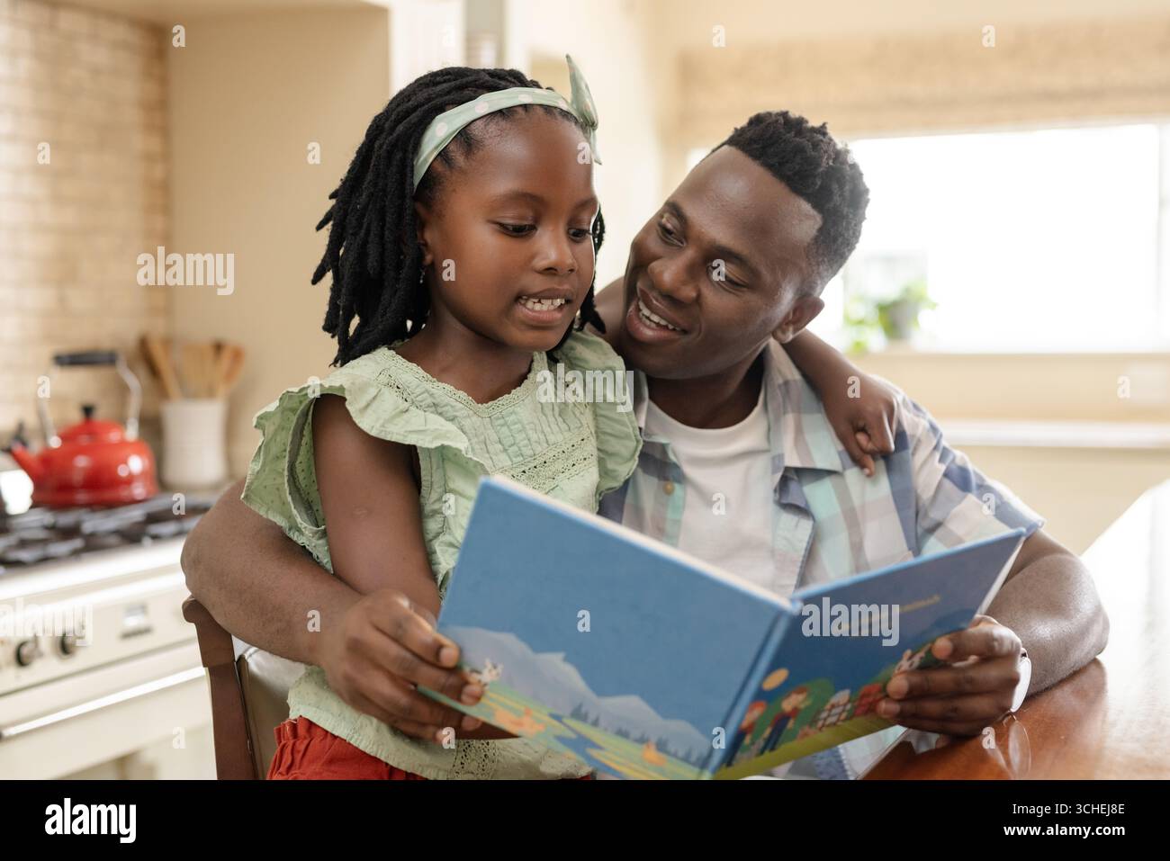 Lecture de livre d'histoires ensemble, père et enfant partageant un moment joyeux à la table de la cuisine Banque D'Images Lecture de livre d'histoires ensemble, père et enfant partageant un moment joyeux à la table de la cuisine Banque D'Images