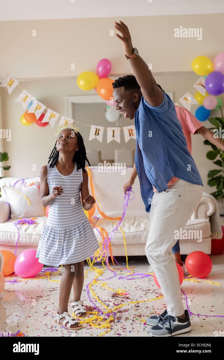 À la fête, père et fille dansant joyeusement à la maison pendant la célébration d'anniversaire colorée Banque D'Images À la fête, père et fille dansant joyeusement à la maison pendant la célébration d'anniversaire colorée Banque D'Images