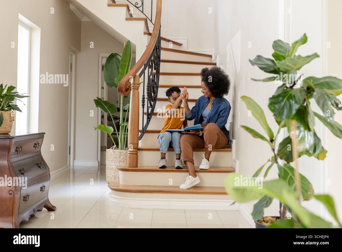Mère afro-américaine et enfant assis dans les escaliers, haut-fving et souriant chaleureusement Banque D'Images Mère afro-américaine et enfant assis dans les escaliers, haut-fving et souriant chaleureusement Banque D'Images