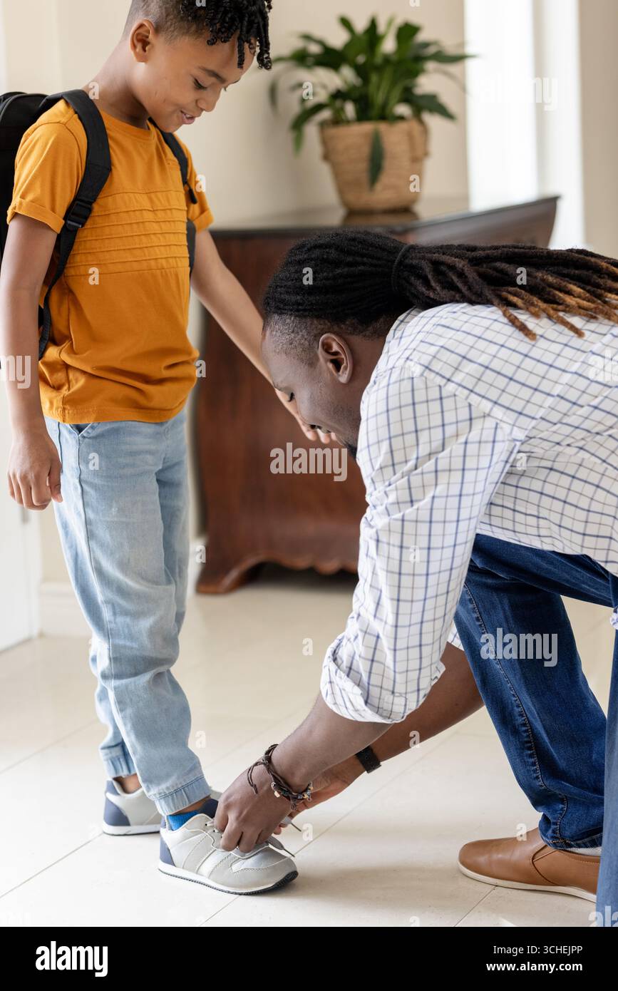 Père attachant la chaussure de son fils à la maison, se préparant à l'école avec un sac à dos Banque D'Images Père attachant la chaussure de son fils à la maison, se préparant à l'école avec un sac à dos Banque D'Images