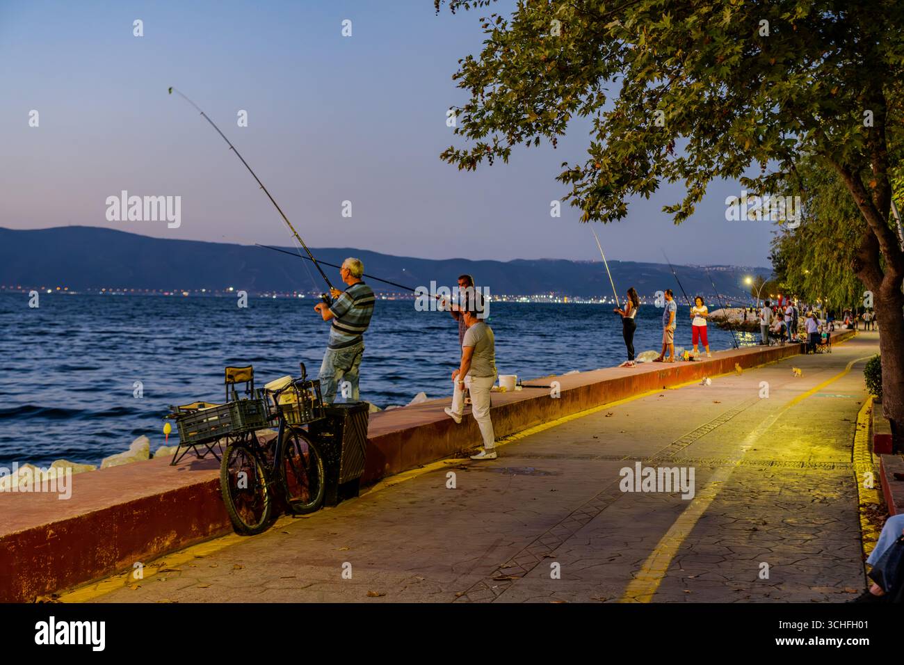Les gens pêchent avec des cannes le long de la promenade du front de mer au crépuscule sur le golfe de İzmit à Karamürsel, Kocaeli, Turquie. Karamürsel, Kocaeli, Turquie – août Banque D'Images