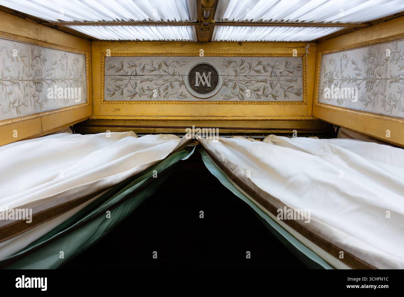 Vue vers le haut de rideaux blancs et verts encadrant un monogramme contre un plafond blanc orné de détails dorés, mettant en valeur la texture luxueuse Banque D'Images