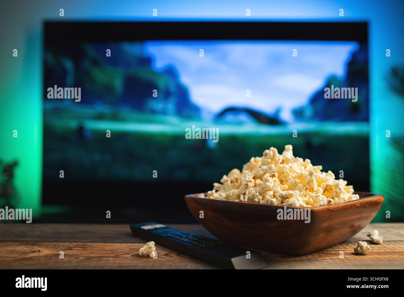 Un bol en bois de pop-corn et une télécommande en arrière-plan le téléviseur fonctionne. Le soir, confortablement assis, regarder un film ou une série télé à la maison. Banque D'Images