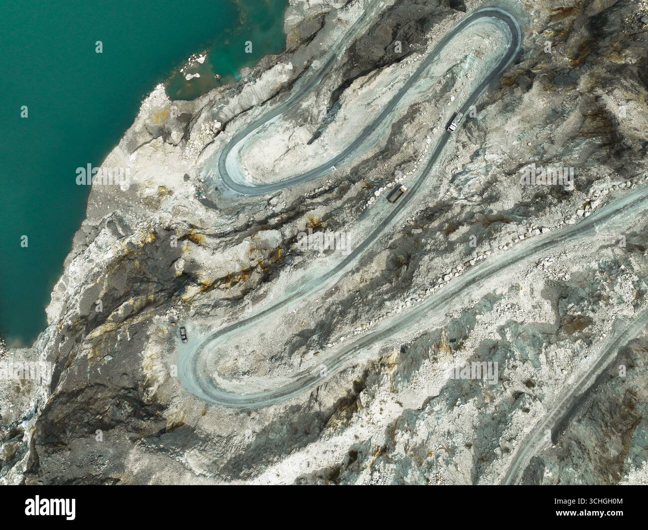 Scène industrielle avec camion en mouvement sur la route sinueuse de carrière, transportant la pierre extraite de la mine à ciel ouvert à l'installation voisine, mettant en évidence la consommation d'énergie, Banque D'Images