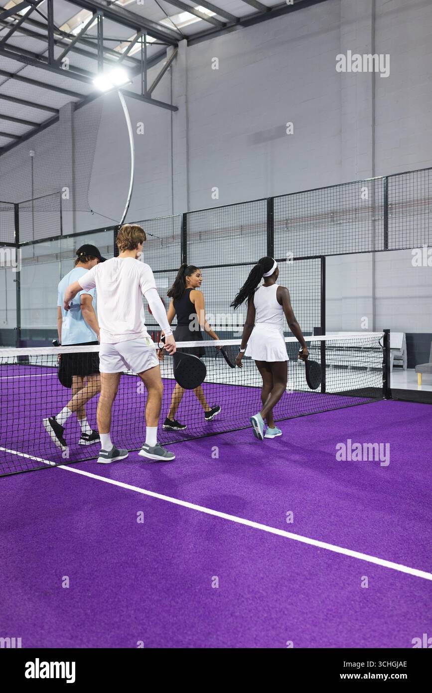 Divers joueurs de padel marchant à travers le filet sur le court violet dans la salle de sport avec escrime, raquettes Banque D'Images